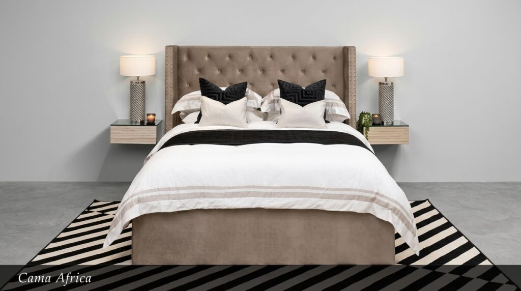 La Cama África combina calidez y elegancia en un tono beige neutro. Su cabecera capitoné con tachuelas y el diseño limpio de la base crean un ambiente acogedor y sofisticado. Los textiles en blanco con rayas beige y cojines negros completan un look equilibrado y moderno.
