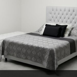 La Cama Ejecutivo transmite lujo y confort superior. Su imponente cabecera capitoné en blanco con botones decorativos domina el espacio, acompañada de un elegante juego de ropa de cama en tonos grises y negros. Incluye un práctico banquito y mesa de noche que completan el conjunto ejecutivo.
