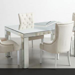El Comedor Reflejo es sinónimo de glamour y modernidad. Su espectacular mesa con base y estructura en espejos combinada con una tapa de cristal crea impresionantes juegos de luz y reflejos en el espacio. Las sillas tapizadas en blanco crema con capitoné y detalles de tachuelas metálicas aportan un toque de lujo y sofisticación.